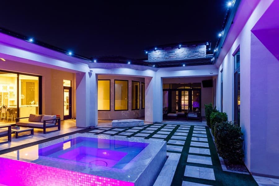 Modern luxury home courtyard with illuminated pool and stylish outdoor seating at night.