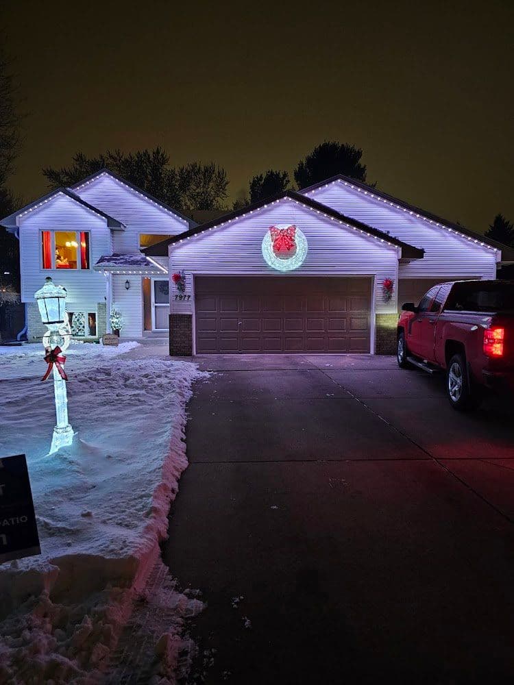 Festive home with Christmas lights, snow, and illuminated decorations at night.