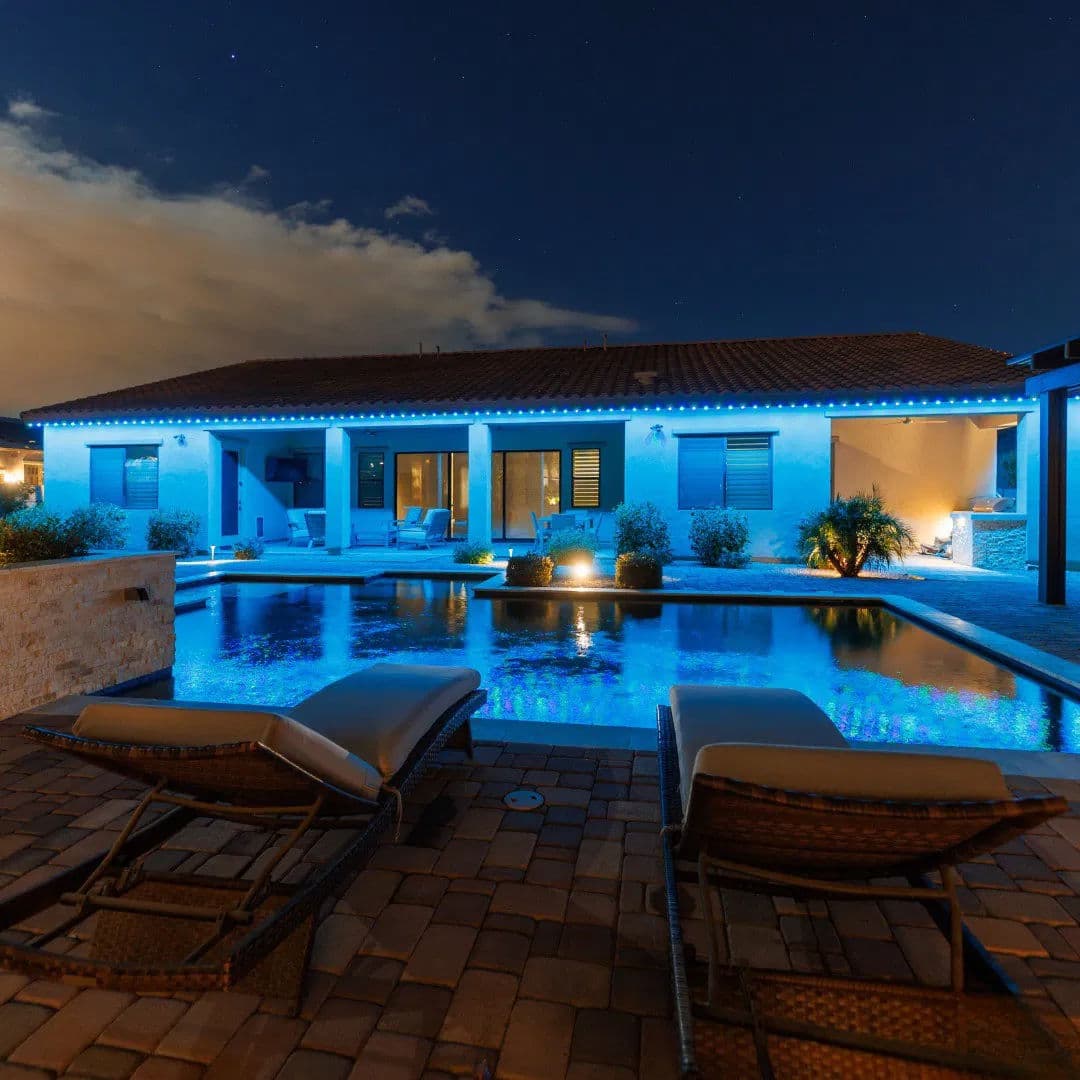 Modern villa at night with illuminated pool and lounge chairs, surrounded by tranquil landscaping.