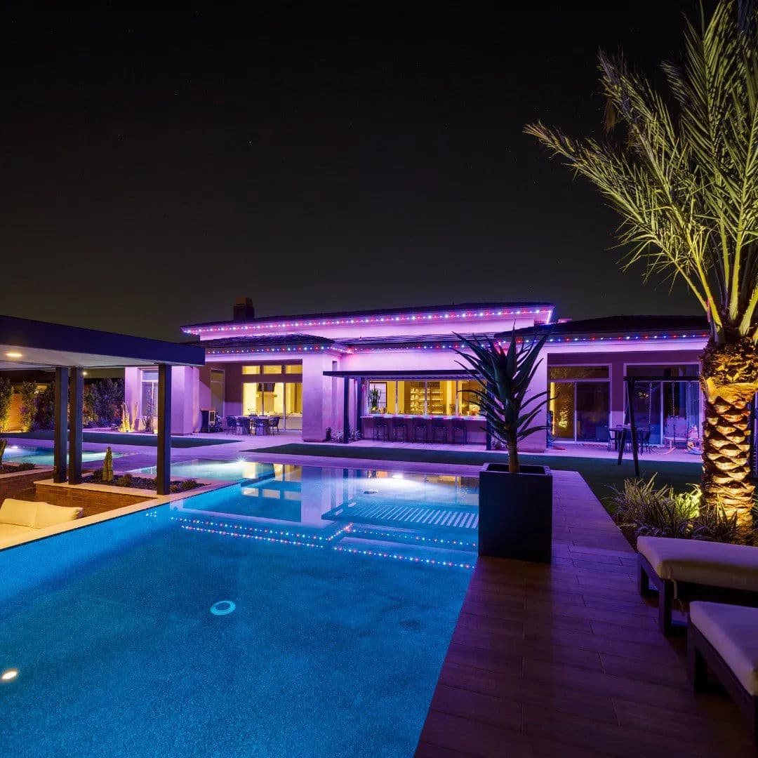 Modern luxury home with illuminated pool and palm trees at night. Romantic outdoor ambiance.