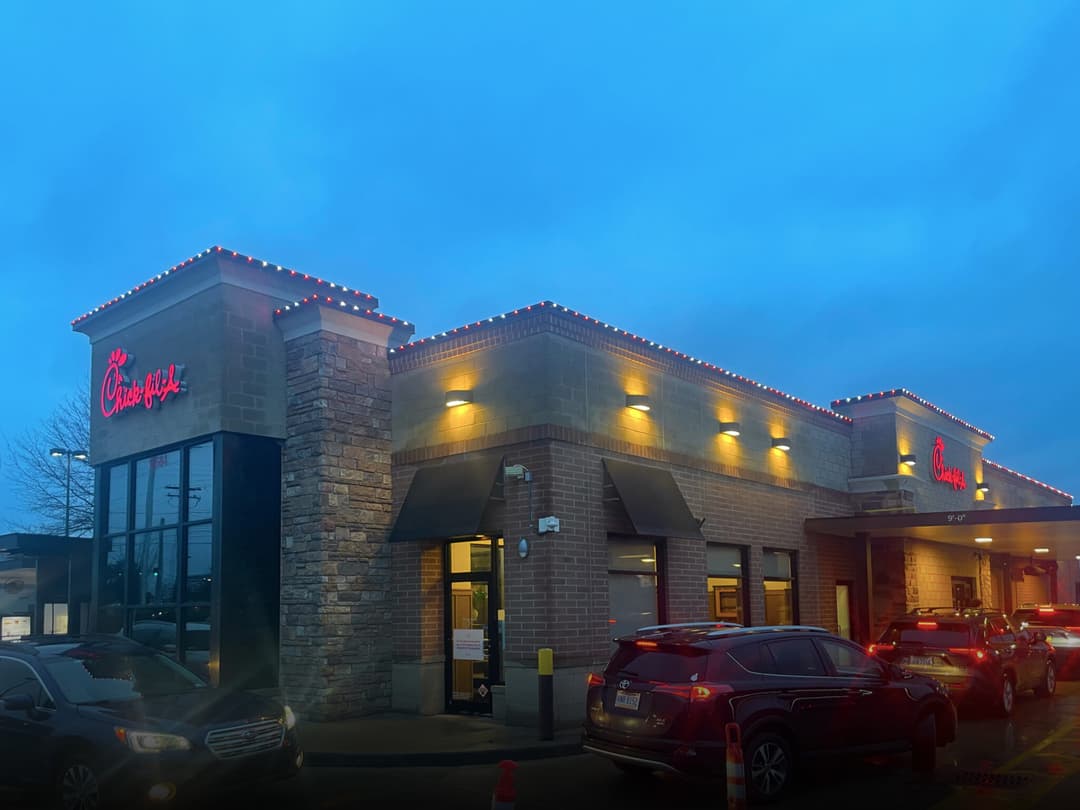 Chick-fil-A restaurant with festive lights and evening sky, featuring cars in drive-thru.