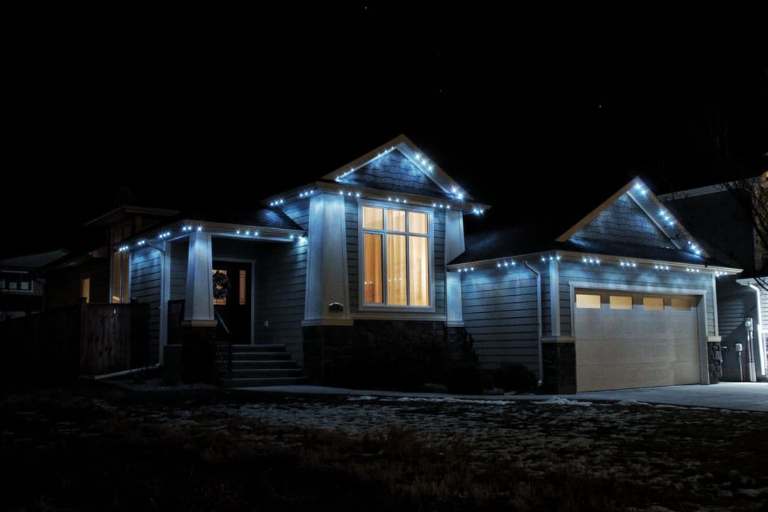 Modern home decorated with blue Christmas lights at night, showcasing a warm glow from windows.