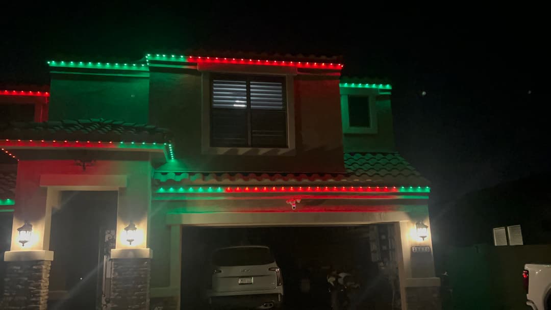 House decorated with red and green holiday lights at night, creating a festive atmosphere.